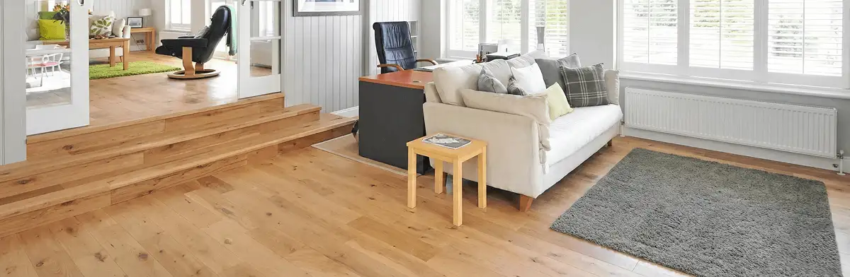 A modern living room with professionally installed laminate flooring, a beige sofa, a small side table, a gray rug, and large windows with white shutters in Grand Rapids, MI